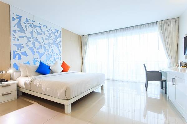 Innenansicht eines Hotelzimmers im Samui Resotel Beach Resort mit weißem Bett, blauen und orangefarbenen Kissen und modernem Design.