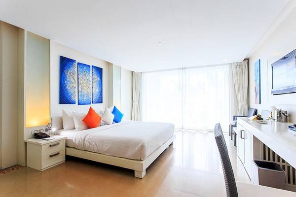 Innenansicht eines Schlafzimmers im Samui Resotel Beach Resort mit einem großen Bett, weißen Möbeln und Kunstwerken an der Wand.
