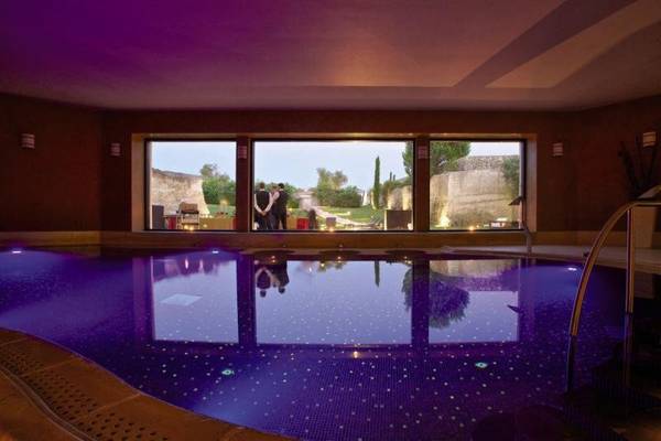 Innenansicht des Pools im MIRA Acaya Golf Resort & SPA mit lila Beleuchtung und Personen am Fenster.