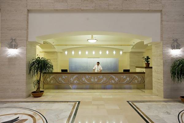 Rezeption des Melas Lara Hotels mit einem Angestellten im Vordergrund und Pflanzen neben dem Empfangstresen.