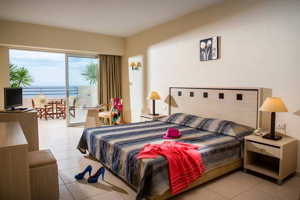 Hotelzimmer im Blue Marine Resort & Spa mit Meerblick, Bett, Nachttischen und Kleidern auf dem Bett.