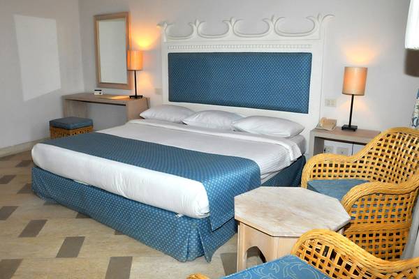 Schlafzimmer im Grand Hotel Sharm El Sheikh mit einem großen Bett, Nachttischen und Korbstühlen.