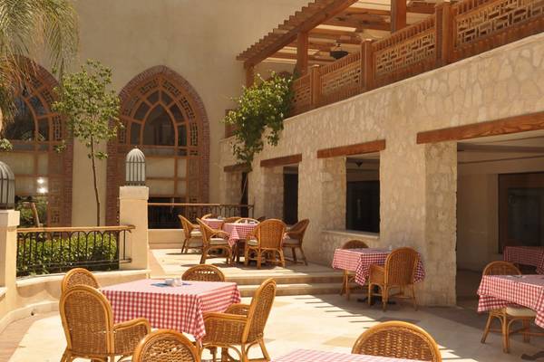 Terrasse des Grand Hotel Sharm El Sheikh mit roten und weißen Tischdecken und Holzstühlen.