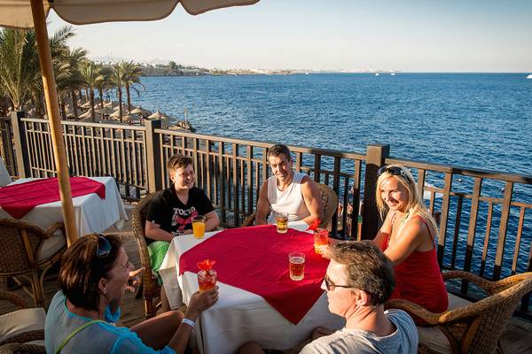 Gruppe von Menschen, die an einem Tisch auf einer Terrasse sitzen und Getränke trinken, während sie den Blick auf das Meer genießen.