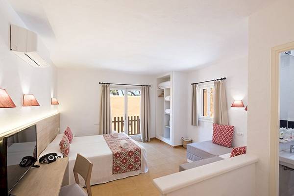 Ein helles Hotelzimmer von Cala Martina by Llum mit einem Doppelbett, Fernseher, Schreibtisch und einer offenen Tür zu einem Balkon.
