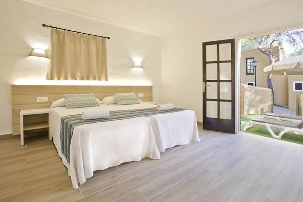 Doppelzimmer im Hotel Cala Martina by Llum mit zwei Betten, weißem Bettlaken und Kissen, einem Nachttisch und einer Tür zum Balkon.