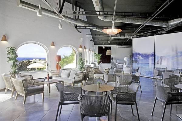 Innenansicht des Cala Martina by Llum Hotels mit Tischen, Stühlen und Pflanzen.