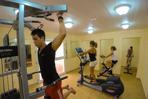 Fitnessstudio im ROC Arenas Doradas Hotel mit drei Personen, die an verschiedenen Geräten trainieren.