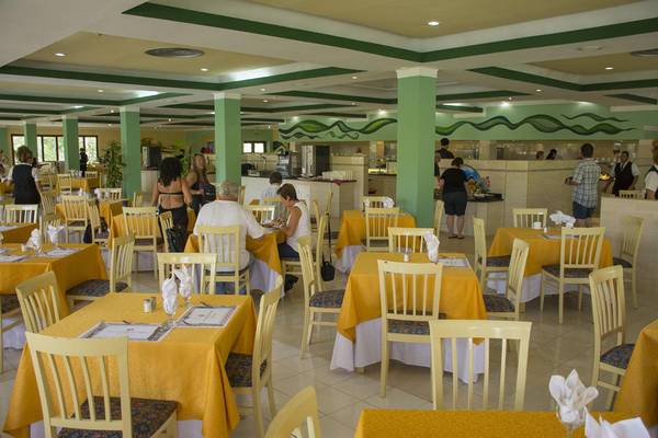 Innenansicht des Restaurants im ROC Arenas Doradas Hotel mit gelbgedeckten Tischen und grünen Säulen.