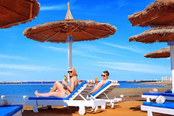 Zwei Personen sitzen unter Sonnenschirmen auf Liegen am Pickalbatros Dana Beach Resort Strand