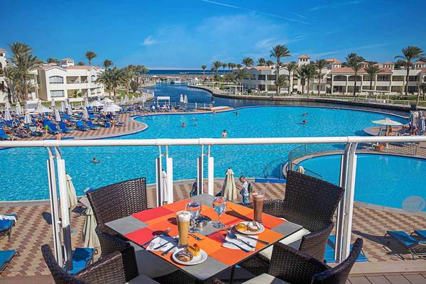 Aussicht auf den Poolbereich des Pickalbatros Dana Beach Resort mit Sonnenliegen und Gebäuden im Hintergrund.