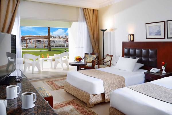 Hotelzimmer mit zwei Betten, Fernseher, Tisch, Stühlen und Terrassenblick auf einen Golfplatz