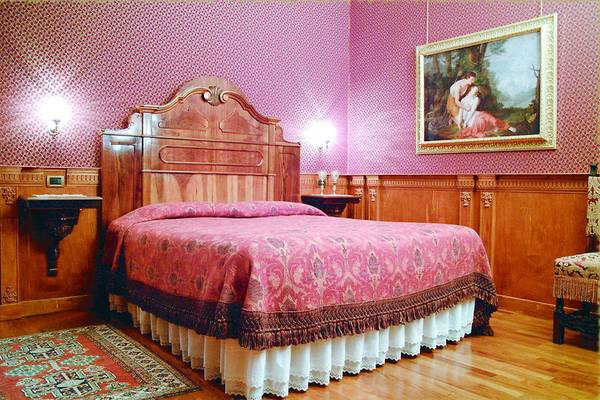 Schlafzimmer im Hotel Casa Nicolo Priuli mit rotem Wandmuster, Holzbett und Gemälde.