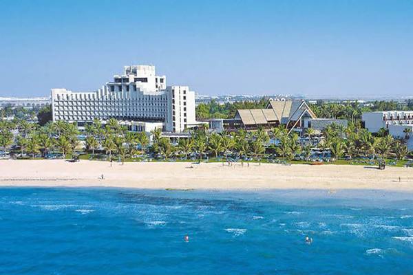 Luftaufnahme des JA Beach Hotels am Strand mit vielen Palmen und Gebäuden im Hintergrund.