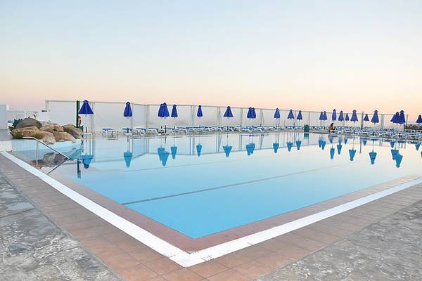 Außenpool des Mastichari Bay Hotels mit blauen Sonnenschirmen und leeren Sonnenliegen.