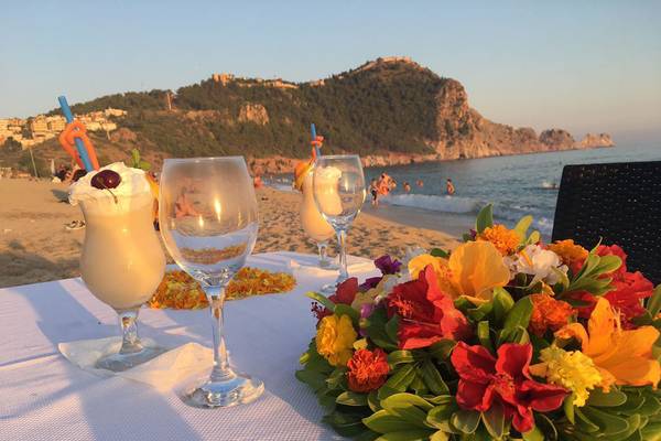 Strandtisch mit Blumen und Getränkegläsern, Blick auf das Meer und eine Klippe