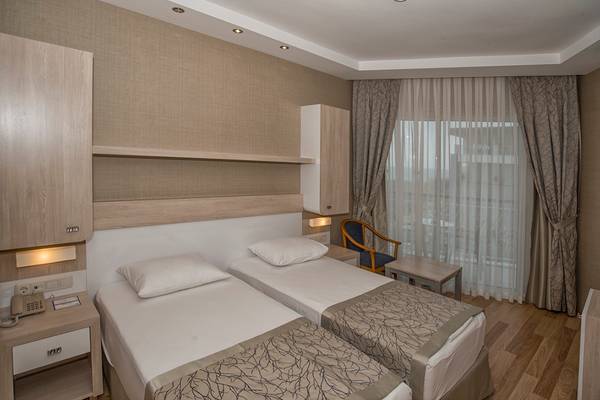 Ein Doppelzimmer im Riviera Hotel & Spa mit zwei Einzelbetten, einem Nachttisch, einem Fenster und Vorhängen.