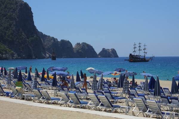 Riviera Hotel & Spa Strand mit vielen Sonnenschirmen und einem Schiff im Hintergrund.
