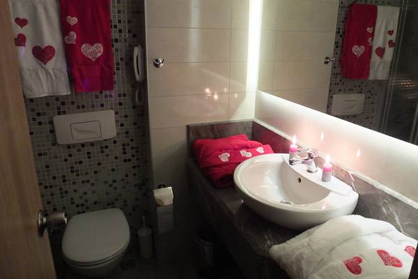 Badezimmer mit roten Handtüchern, weißen Bademänteln und zwei brennenden Kerzen im Hotel Riviera & Spa.