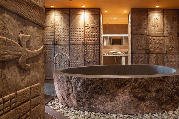 Ein Badezimmer im Lopesan Baobab Resort mit einer großen Steinbadewanne, umgeben von steinernen Wänden.