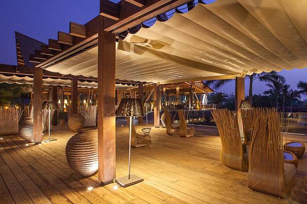 Terrasse des Lopesan Baobab Resorts mit Holzboden, Bambusstühlen und einer großen Markise.