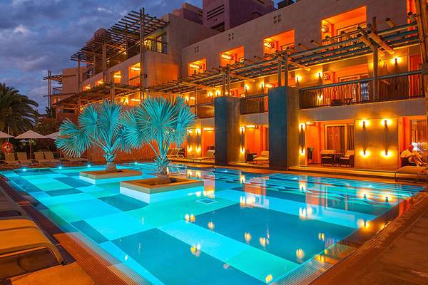 Beleuchteter Swimmingpool des Lopesan Baobab Resorts am Abend mit Loungeliegen und Palmen.
