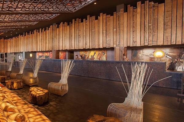 Innenbereich des Lopesan Baobab Resorts mit Holzwänden, Sitzgelegenheiten und einem langen Empfangstresen.