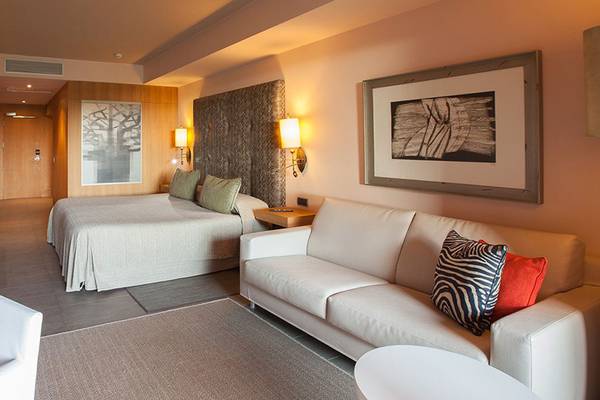 Innenansicht des Lopesan Baobab Resort Hotels, zeigt ein Schlafzimmer mit Bett, Couch, Schreibtisch und Gemälde.