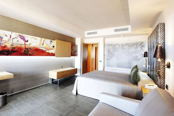 Hotelzimmer im Lopesan Baobab Resort mit moderner Einrichtung, Kunstwerk an der Wand, Bett, Schreibtisch, Stuhl und Telefon.
