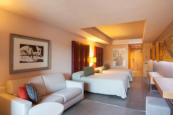 Innenansicht eines Zimmers im Lopesan Baobab Resort mit einem Sofa, zwei Betten, Gemälden und Lampen.