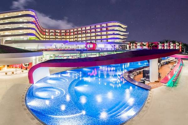 Temptation Cancun Resort Pool bei Nacht mit leuchtenden Farben und Gebäuden im Hintergrund