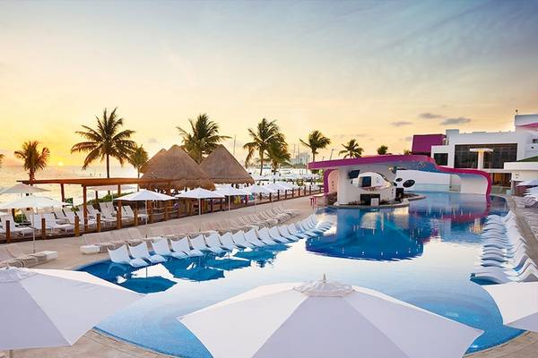 Temptation Cancun Resort Pool bei Sonnenuntergang mit vielen Liegestühlen und Sonnenschirmen