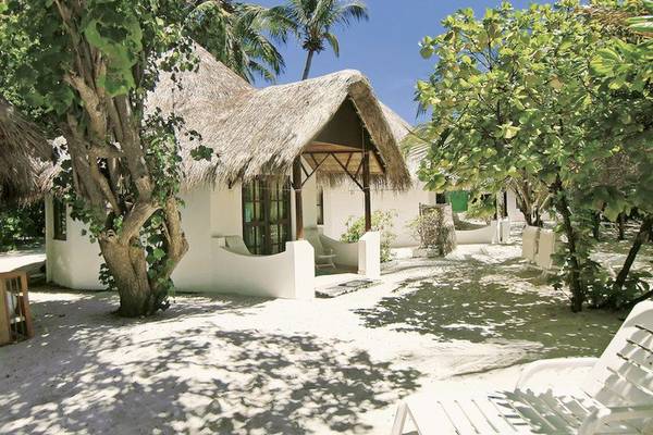 Bungalow des Thulhagiri Island Resorts mit Strohdach, umgeben von Bäumen und weißen Möbeln.