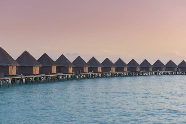 Reihe von Hütten auf Stelzen im Thulhagiri Island Resort bei Sonnenuntergang