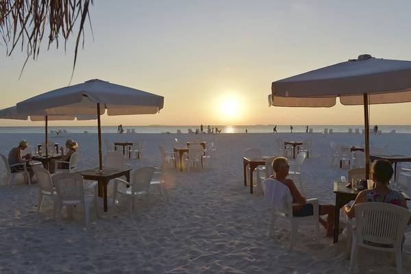 Gaste sitzen bei Sonnenuntergang unter Sonnenschirmen auf der Thulhagiri Island Resort Strand