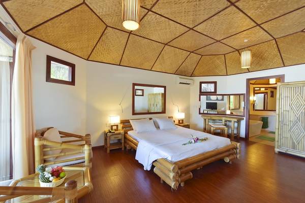 Innenansicht eines Schlafzimmers im Thulhagiri Island Resort mit Bett, Holzmöbeln und Blumen.