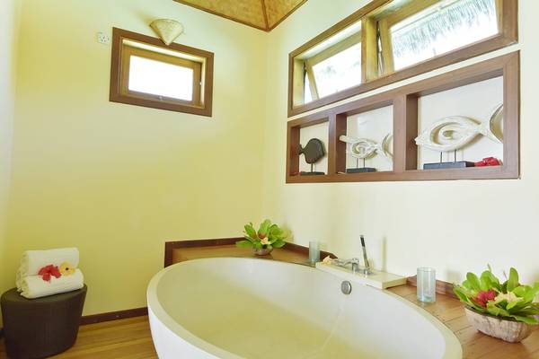 Badezimmer im Thulhagiri Island Resort mit Badewanne, Blumen und Holzmöbeln.