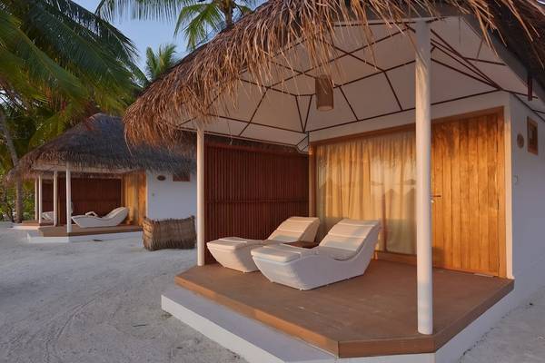 Strandhütten des Thulhagiri Island Resorts mit weißen Liegestühlen und Strohdächern auf einem weißen Sandstrand.