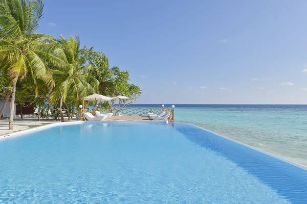 Außenpool des Thulhagiri Island Resorts mit Liegestühlen und Sonnenschirmen am Strand.