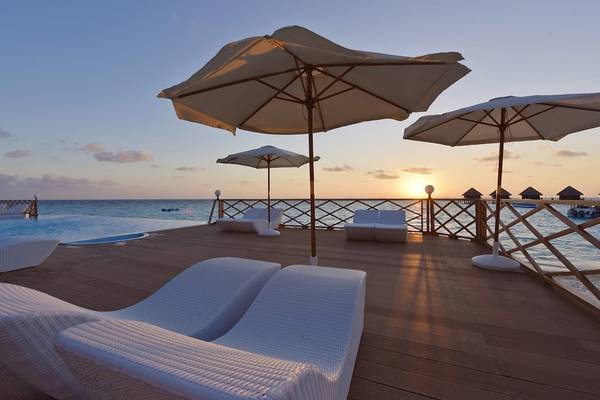 Terrasse des Thulhagiri Island Resorts bei Sonnenuntergang mit Sonnenschirmen und Liegen am Pool