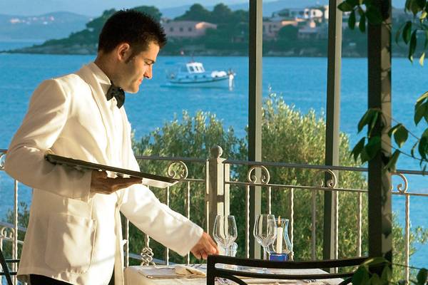 Kellner im weißen Anzug steht auf der Terrasse des Gabbiano Azzurro Hotel & Suites und serviert eine Mahlzeit mit Blick auf das Meer.