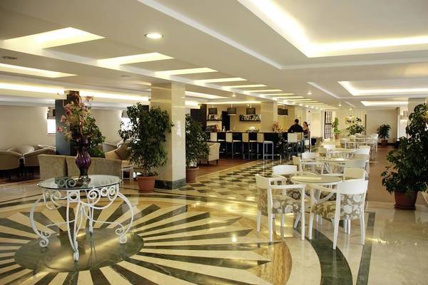 Der elegante Innenbereich des Monachus Hotel & Spa mit gemusterten Bodenfliesen, weißen Tischen und Stühlen und einigen Pflanzen.