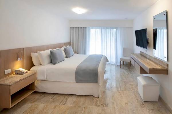 Viva Wyndham Dominicus Palace Hotelzimmer mit weißem Bett, grauen Kissen und Fernseher.
