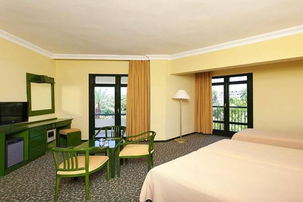 Doppelzimmer im Miramare Beach Hotel mit zwei Betten, grünen Stühlen, Tisch und Fernseher auf dem Schreibtisch.