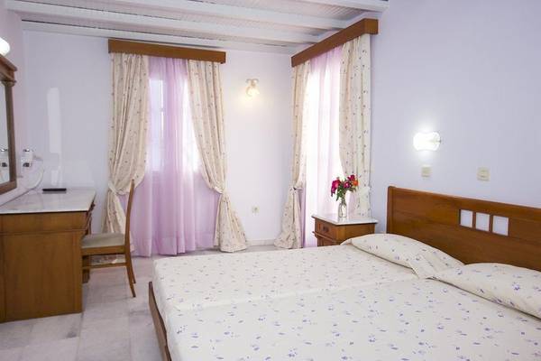 Schlafzimmer mit einem Bett, zwei Kissen, einem Schreibtisch, einem Stuhl, einem Spiegel und einer Vase mit Blumen.