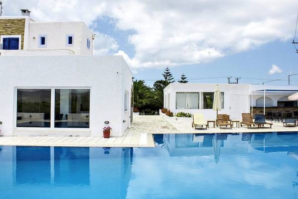 Weißes Hotel Naxos Holidays mit Pool und Lounge-Stühlen im Freien.
