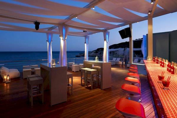 Terrasse des Proteas Blu Resorts bei Nacht mit Blick auf das Meer und roten Stühlen.