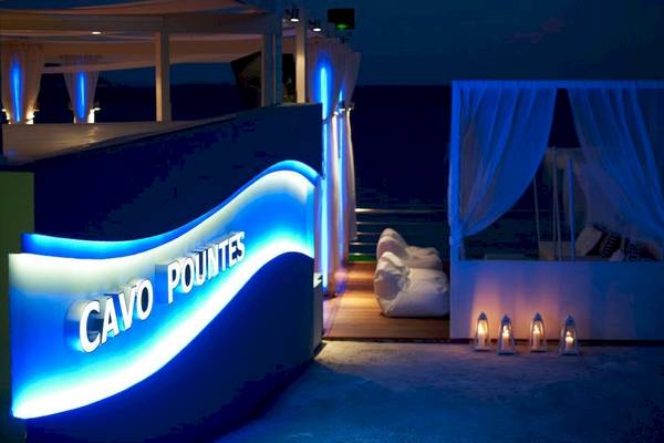 Terrasse des Proteas Blu Resorts mit blauen Lichtern und einem Schild, das 'Cavo Pountes' in weißer Schrift auf blauem Hintergrund beleuchtet.