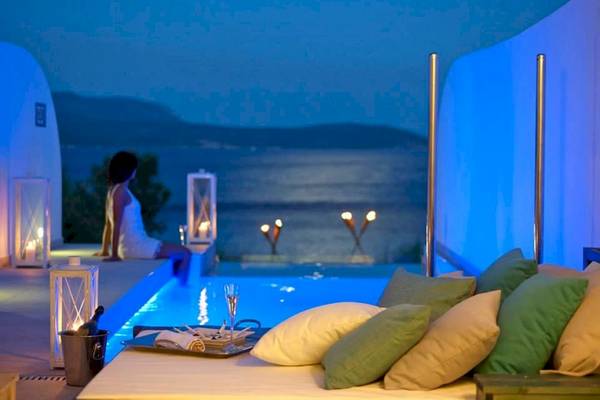 Nachtansicht des Proteas Blu Resorts mit einer Person, die an einem Swimmingpool sitzt, umgeben von Laternen und Blick auf das Meer.