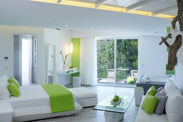 Innenansicht eines Zimmers im Proteas Blu Resort mit weißer und grüner Farbgebung, Bett, Wohnbereich und Terrasse.